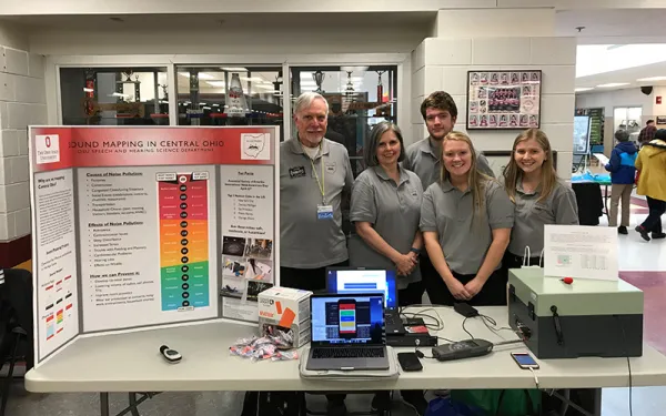 Faculty and students with research poster and research equipment in table fair setting